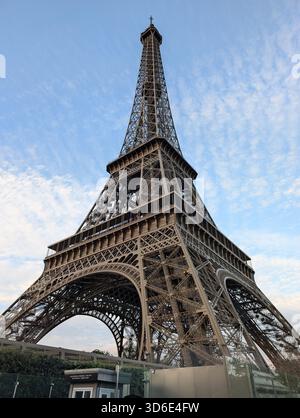 Der Eiffelturm in Paris, Frankreich, wurde aus einem niedrigen Winkel fotografiert, mit seiner eisernen Gitterstruktur, die sich in einen blauen, leicht bewölkten Himmel erhebt. Ein klarer Tag Stockfoto