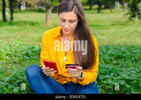 Lächelnde Frau mit Smartphone und Kreditkarte im Sitzen. Stockfoto