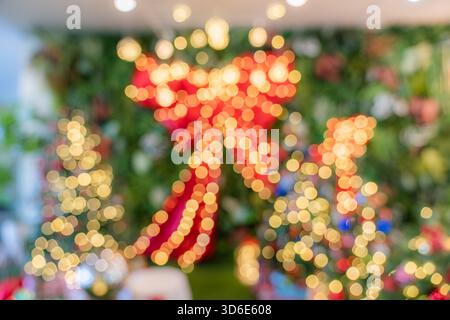 Das Bild zeigt verschwommene Weihnachtslichter, die runde gelbe und rote Bokeh-Formen bilden, mit einer großen roten Schleife und dekorativen Bäumen im Hintergrund. Stockfoto