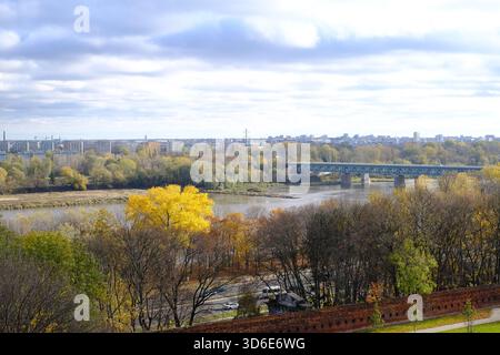 Weitläufiger Blick von der Warschauer Altstadt auf die Weichsel, herbstliche Bäume und eine lange Stahlbrücke unter zerbrochenen Wolken. Stockfoto