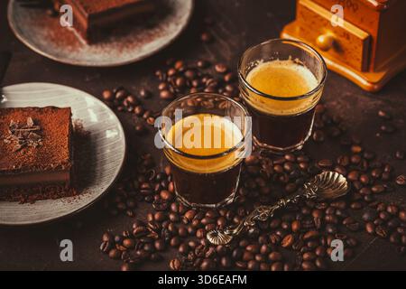 Zwei Espresso-Kaffeetassen mit einem Stück Schokoladenkuchen auf braunem Hintergrund Stockfoto