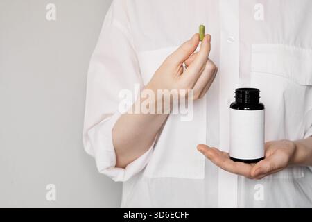 Frau mit grüner Naturkapsel und leerer Vitaminflasche, die das Wohlbefinden fördert Stockfoto