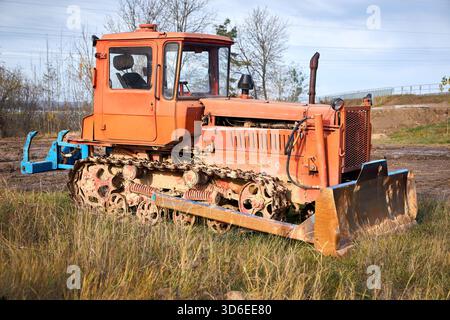Alte orange, rostige, schmutzige Landwirtschafts-Raupenschlepper-Bulldozer in ländlicher Herbstlandschaft Stockfoto