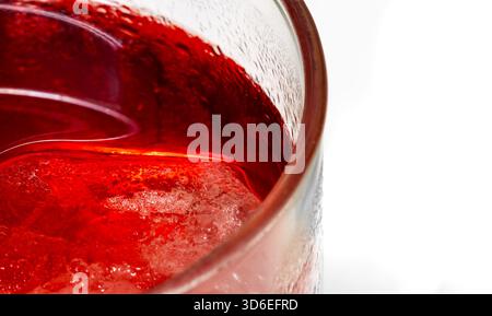 Makroaufnahme mit der intensiven roten Farbe und Textur eines kalten Getränks, die glatte Flüssigkeitsoberfläche, einen untergetauchten Eiswürfel und einen winzigen Wassertropfen zeigt Stockfoto