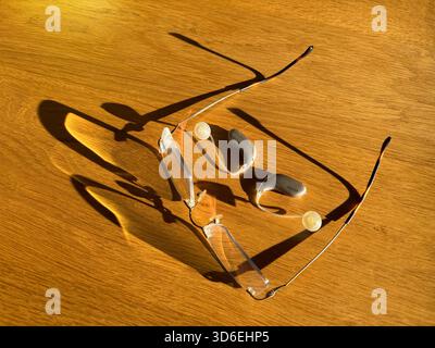 Brillen und Hörgeräte auf Holztisch bei stürmischem Sonnenlicht. Stockfoto