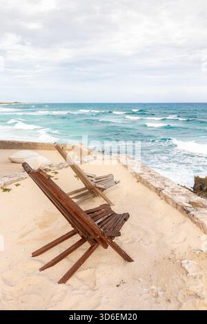 Zwei rustikale hölzerne Liegestühle mit Blick auf das türkisfarbene Karibische Meer an einem Sandstrand in Cozumel, Mexiko, einem idyllischen und ruhigen tropischen Ort Stockfoto