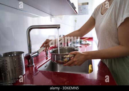 Frau, die einen Topf mit Wasser am Waschbecken in einer modernen Küche füllt. Die Umgebung unterstreicht einen lässigen Lebensstil zu Hause und konzentriert sich auf echte Kochkünste Stockfoto