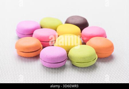 Eine lebendige Auswahl traditioneller französischer Macarons auf einer strukturierten Matte. Diese zarten Kekse bestehen aus Eiweiß, Puderzucker, Mandeln, Stockfoto
