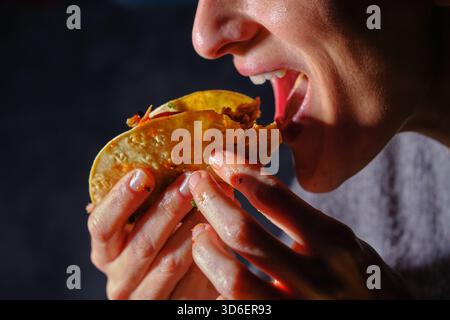 Ein zugeschnittenes, nicht erkennbares Nahaufnahme-Bild, das eine Frau einfängt, während sie in einen geschmackvollen Ripptako beißt. Ihre Finger greifen den Taco fest und heben den hervor Stockfoto