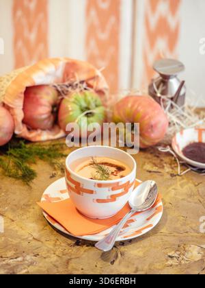 Authentische Gazpacho, eine klassische spanische kalte Suppe, serviert in einer gemusterten Schüssel auf natürlicher Holzoberfläche, begleitet von frischen Zutaten. Stockfoto