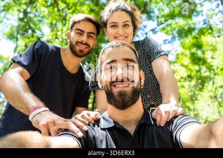 Zwei Männer und eine Frau stehen zusammen und lächeln draußen in einem üppigen grünen Park in die Kamera, symbolisieren Freundschaft und Freude Stockfoto