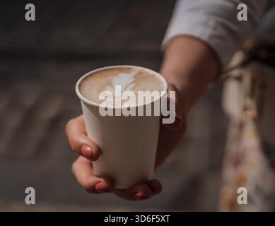 Warme Tasse cremigen Kaffee, gehalten von einer Hand in einem sonnigen Außenbereich an einem entspannten Nachmittag Stockfoto