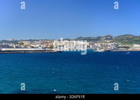 Weite Küstenlandschaft mit Ceuta, Hafeninfrastruktur und bergigem Gelände dahinter. Stockfoto