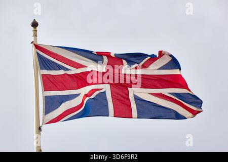Union Jack Flag fliegt auf dem Pole gegen den hellen Himmel, Symbol für Großbritannien und Stolz Stockfoto