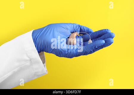Arzt mit Hörgerät auf gelbem Hintergrund, Nahaufnahme Stockfoto