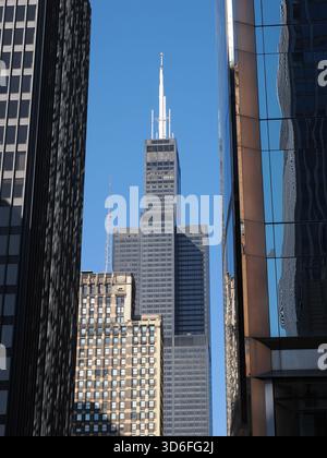 Chicago, IL - 16. September 2025: Der Willis Tower ist durch die enge Lücke zwischen zwei dunklen und stark reflektierenden zeitgenössischen Wolkenkratzern sichtbar. Stockfoto