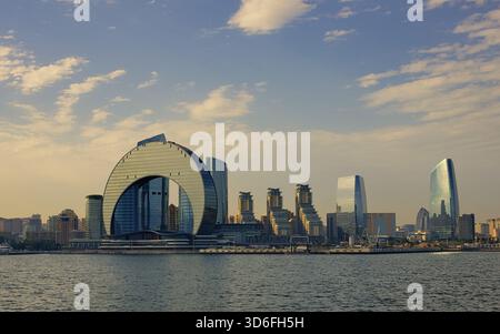Ein abendlicher Blick auf Bakus moderne Stadtlandschaft mit dem ikonischen halbmondförmigen Wolkenkratzer und den Gebäuden am Wasser entlang des Kaspischen Meeres. Aserbaidschan Stockfoto