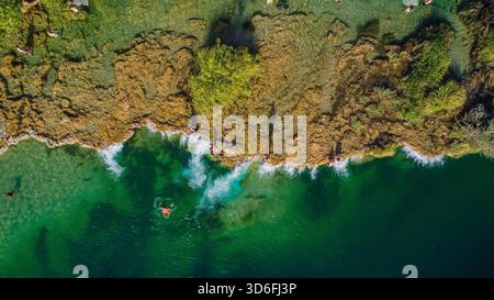 Direkter Blick von oben auf eine lebendige natürliche Travertinbarriere mit Schwimmern, die das smaragdgrüne und türkisfarbene Wasser genießen Stockfoto