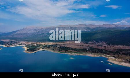 Panoramablick auf die massiven, geschichteten Hänge des Mount Dinara, die auf das tiefblaue Wasser des Stausees Peruća in Kroatien treffen Stockfoto