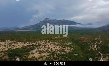 Die Berglandschaft auf dem Balkan ist von Nebel und dunklen Wolken umgeben, von einer Rauchsäule, die vom zerklüfteten Gipfel aufsteigt Stockfoto