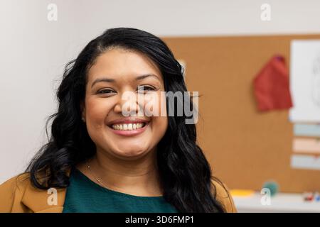 Frau, die im Büro steht und einen Blazer trägt, der Stressball an Korkbrett mit festgehaltenem rotem Tuch hält Stockfoto