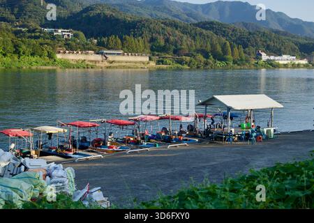 Kleine Angel- und Ausflugsboote mit roten Baldachinen liegen an einem Pier am Fluss North Han bei Gapyeong, mit bewaldeten Bergen und Dorf Lo Stockfoto