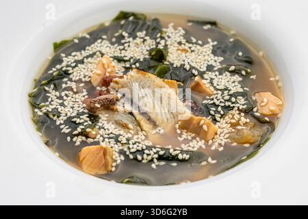 Miso-Suppe mit Lachs, Wakam und Sesam in weißer Schüssel auf dunklem Steintisch Stockfoto