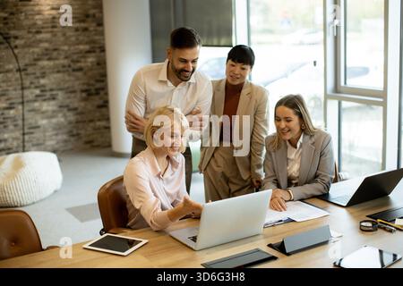 Gruppe von vier Fachleuten, die in einem eleganten Büro zusammenarbeiten. Sie diskutieren ein Projekt, während sie sich einen Laptop-Bildschirm ansehen und Teamwork A zeigen Stockfoto