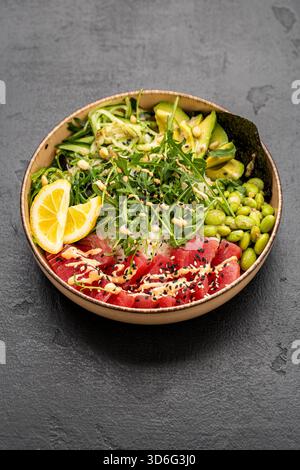 Bunte Thunfisch-Poke-Schüssel mit Reis Avocado Edamame und Sesam auf dunklem Steinhintergrund Stockfoto