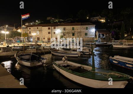 Eine ruhige Nachtszene in einem Hafen mit kleinen Booten, die an einem Steinkai anlegen, warmer Straßenbeleuchtung und traditionellen Dorfgebäuden, die Ruhe widerspiegeln Stockfoto