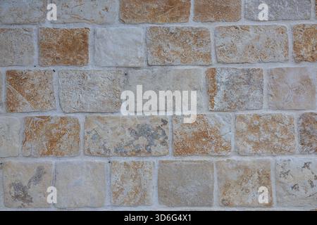 Eine verwitterte graue Steinmauer aus unregelmäßigen Felsen, die mehrschichtiges Mauerwerk und Anklänge von trockenem Gras im Vordergrund zeigt. Ideal für rustikale Architektur Stockfoto