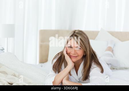Weiße Bettwäsche und gemusterte Überwürfe schaffen eine weiche, minimalistische Schlafzimmerszene nahe transparenter Vorhänge. Ruhe, Ruhe, Entspannung, gemütlich, Komfort, natürlich, Stockfoto