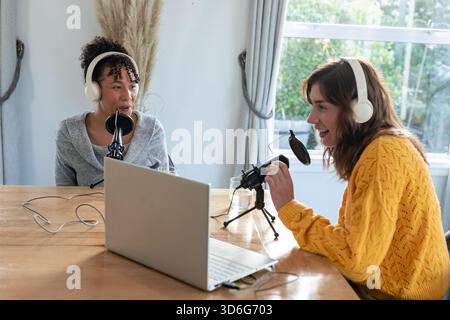 Verschiedene Freundinnen, die Podcasts im Home Office mit Laptop-Mikrofonen mit Pop-Filtern aufnehmen Stockfoto