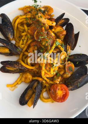 Blick auf einen runden Teller italienischer Meeresfrüchte-Pasta, garniert mit einer halben Tomate auf einem Trattoria-Tisch in Italien. Stockfoto