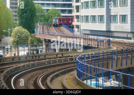London, Vereinigtes Königreich - 18. Mai 2023: Docklands Light Railway oder DLR U-Bahn, Ankunft auf gekrümmter Bahn, Gebäude in der Nähe. Stockfoto