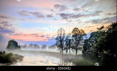 Nebliger Sonnenuntergang über einem ruhigen Fluss Isla in der Nähe von Blairgowrie in Perthshire, Schottland, und Herbstbäume spiegeln sich im Wasser und sanfter Nebel Stockfoto