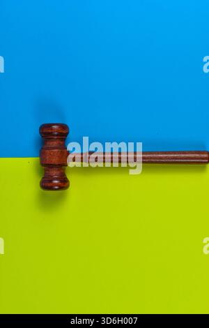 Hölzerner richterlicher Hammer auf blauem und gelb-grünem Hintergrund, der Recht, Gerechtigkeit und Autorität in einer optisch eindrucksvollen Komposition symbolisiert. Stockfoto