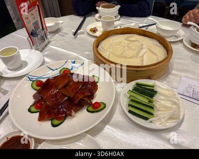 Peking in Scheiben geschnittene Ente, serviert mit dünnen Pfannkuchen, Gurke, Frühlingszwiebeln und Hoisin-Sauce auf einer weißen Tischdecke in einem traditionellen Restaurant. Stockfoto