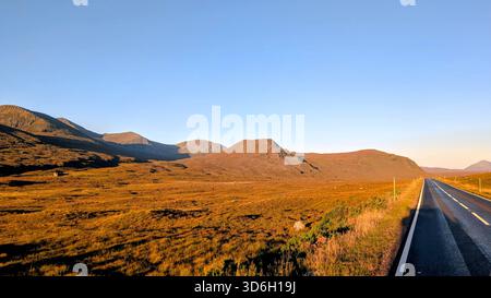Morgenlicht über der A835 in der Nähe von Loch Glascarnoch, mit weiten offenen Mooren und Highland Mountains, die in warmer Sonne leuchten auf dem Weg nach Ullapool Stockfoto