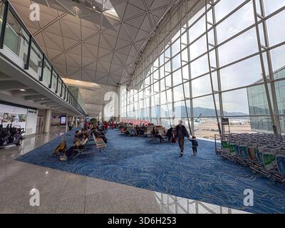 Hong Kong International Airport. Modernes Terminal-Interieur mit wartenden Passagieren, einem Mann und einem Kind, das auf dem Weg ist, und großen Fenstern mit Blick auf den Flugplatz Stockfoto