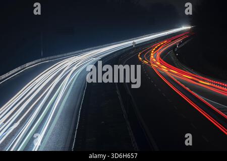 Abstraktes Bild von Nachtverkehrsampeln auf der Straße. Leichte Autofahrten bei Nacht auf kurvenreichen Asphaltstraßen. Langzeitbelichtung zeigt Bewegungen von Autos aus bridg Stockfoto