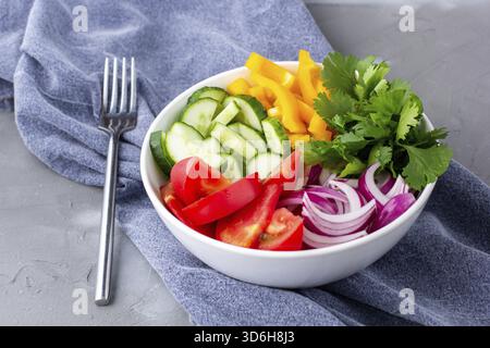 Essen, Teller mit Regenbogensalat mit verschiedenen Gemüse und Kräutern in weißer Schüssel mit Gabel und Serviette auf grauem Steinhintergrund Stockfoto