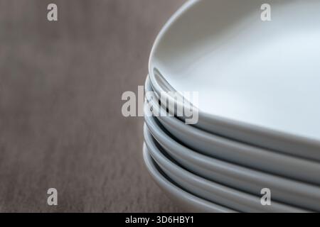 Stapel von rechteckigen weißen Keramikschalen mit abgerundeten Kanten. Set Gruppe von klassischen Porzellan glänzend saubere Schalen. Gestapelte quadratische Platten auf Holz b Stockfoto