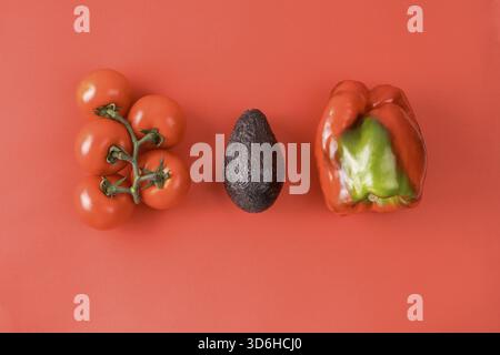Layout aus Avocado, Tomate und Pfeffer. Lebensmittelkonzept. Gemüse auf rotem Hintergrund. Minimales Sommerkonzept. Gemüsedesign. Flache Lagen Stockfoto
