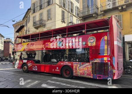 Mailand, Italien - 11. April 2025: Roter City Sightseeing Bus mit farbenfrohen Grafiken auf der Straße in der Nähe klassischer gelber Gebäude. Offenes Dach, historisches zentrum Stockfoto