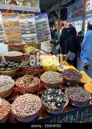 Farbenfrohe Ausstellung von getrockneten Kräutern, Gewürzen und Blumen in Metallschalen im geschäftigen traditionellen Gewürzmarkt Souk & Leute spazieren im Hintergrund Dubai VAE Stockfoto