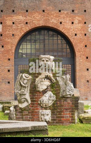 Sammlung von antiken Steinschnitzereien vor dem Hintergrund eines roten Ziegelbogens und einer roten Mauer Stockfoto
