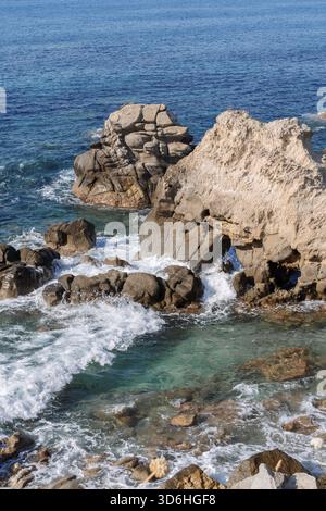 Wellen am felsigen Strand, Meer mit Wellen, die über die großen Felsen brechen, sonniger Sommertag Stockfoto
