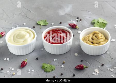 Essen, Set mit verschiedenen Soßen mit Gewürzen auf grauem Steinhintergrund. Mayonnaise Ketchup Senf. Kopierbereich Stockfoto