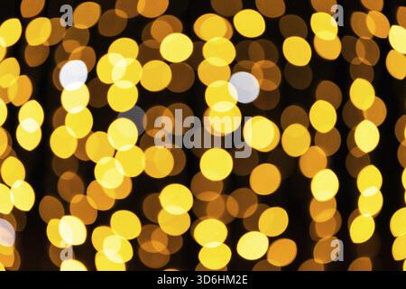 Abstrakte goldene Bokeh-Lichter schaffen eine warme und festliche Atmosphäre vor dunklem Hintergrund, perfekt für Feiern oder Feiertage Stockfoto